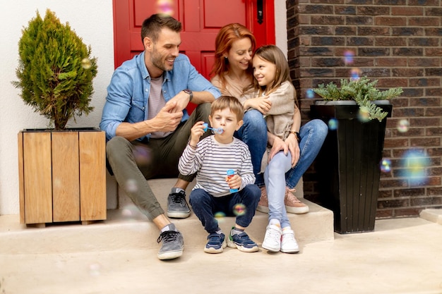 Family with a mother father son and daughter sitting outside on the steps of a front porch of a brick house