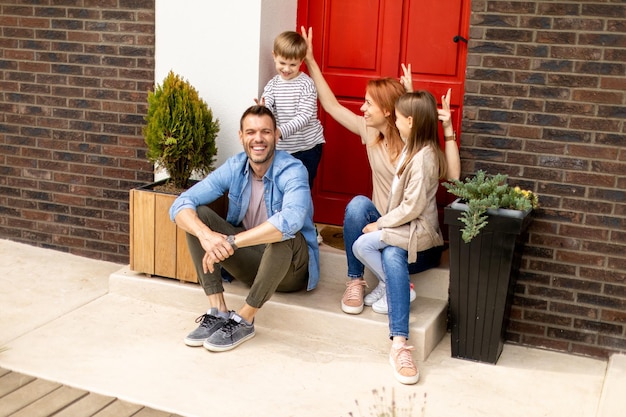 Photo family with a mother father son and daughter sitting outside on the steps of a front porch of a brick house