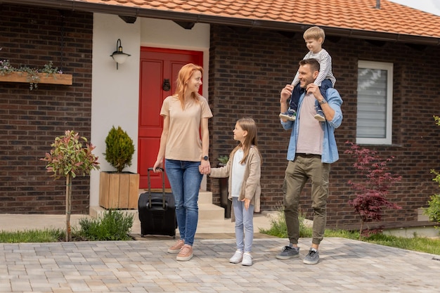 Family with a mother father son and daughter walking with baggage outside on the front porch of a brick house