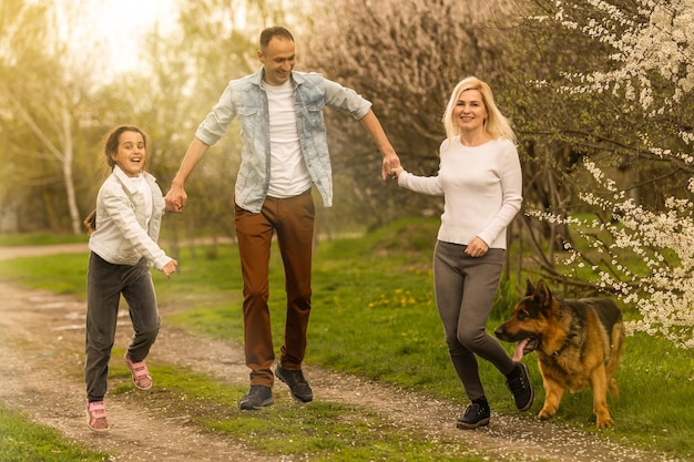 Family with small child and dog outdoors in orchard in spring.