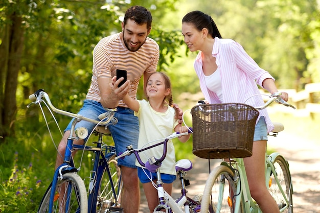 family with smartphone and bicycles in summer park