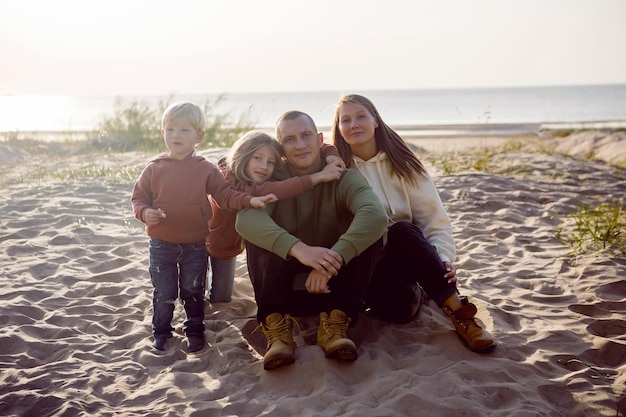 Photo family with a son and daughter and a dog sit on the sand in autumn