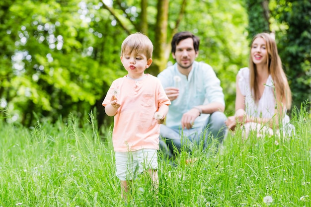 Foto famiglia con figlio sul prato che soffia fiore di tarassaco