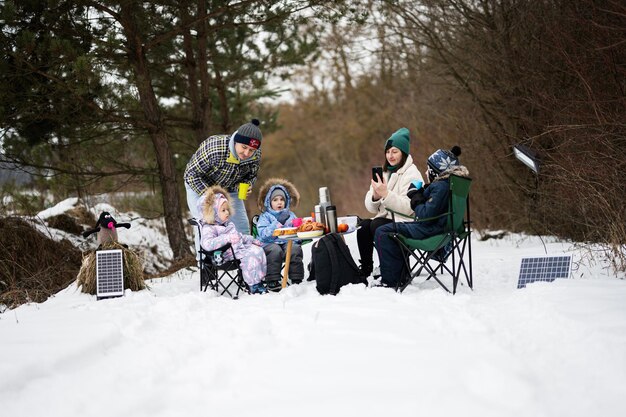 Famiglia con tre bambini nella foresta invernale che trascorrono del tempo insieme durante un picnic