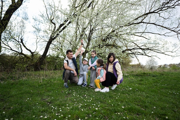 Family with three kids in spring meadow on the background of a flowering tree