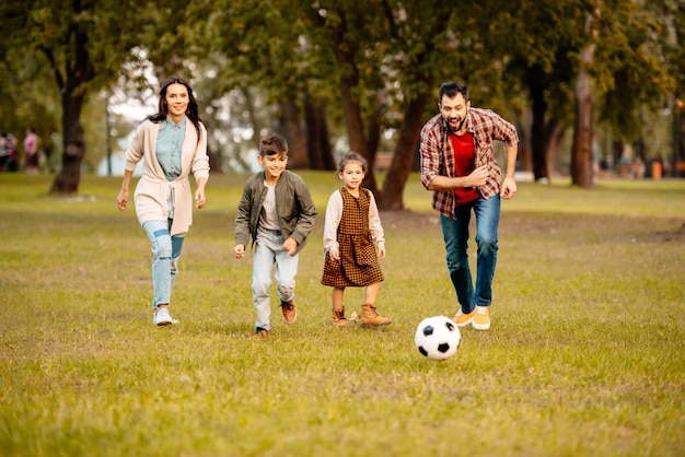 Family with two children playing football together in an autumn park