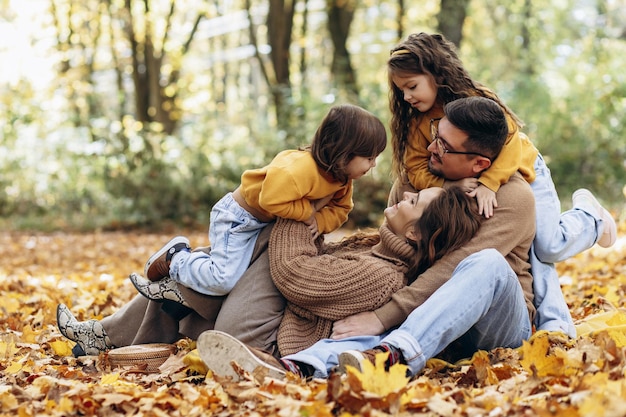 Family with two daughters sitting in park in autumn leaves