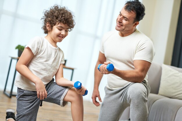 Family workout sportive latin middle aged father teaching his son exercising with dumbbells while