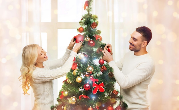 семья, рождество, зимние праздники и концепция людей - счастливая пара украшает елку дома над огнями
