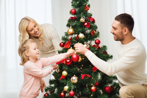 가족, 엑스마스, 겨울 방학, 그리고 사람들의 개념 - 행복한 어머니, 아버지, 그리고 집에서 크리스마스 트리를 장식하는 어린 딸