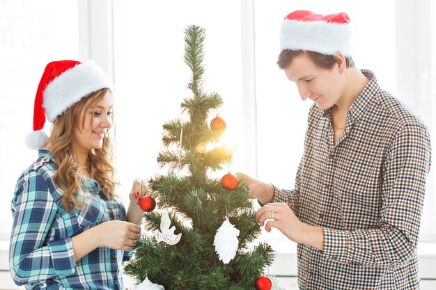 Family, x-mas, winter holidays and people concept - happy young couple decorating christmas tree at home.