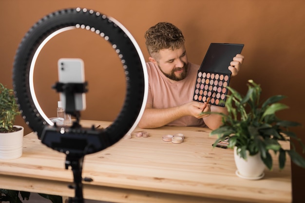 Известный блоггер Веселый влогер-мужчина показывает косметические продукты во время записи видео и дает советы для своего блога о красоте Визажист и запись концепции блога о красоте