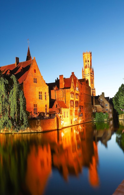 Famous view of Bruges tourist landmark attraction Rozenhoedkaai canal with Belfry and old houses along canal with tree in the night Belgium