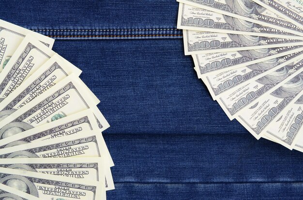 The fan of a lot of US dollars is on a dark denim surface. Background image