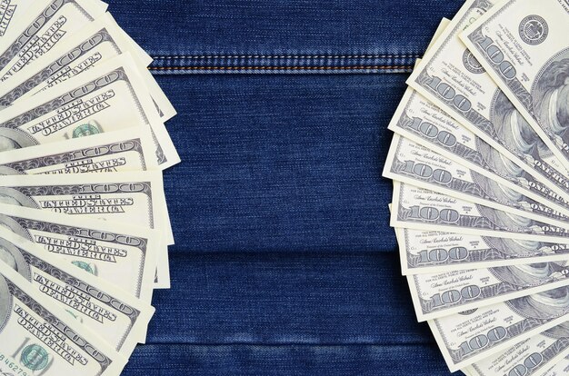 The fan of a lot of US dollars is on a dark denim surface. 