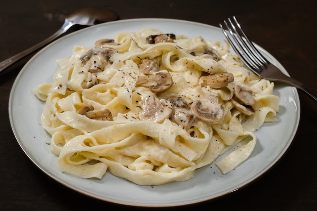 Fancy biologische fetuccine pasta met romige Alfredo champignonsaus. Rustiek bord en donker oppervlak.
