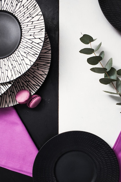 Fancy plates on black and white background. Creative restaurant table setting with flowers and purple color accents