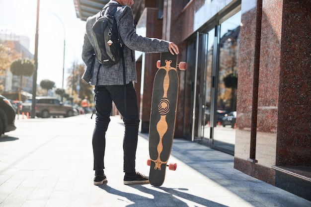 a fancy senior gentleman leaning on his longboard while standing in the street