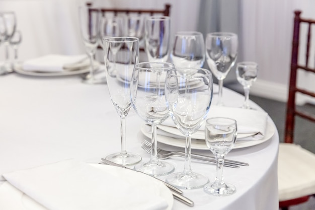 Fancy table set for dinner with napkin glasses in restaurant, luxury interior table. Wedding elegant banquet decoration and items for food arranged by catering service on white tablecloth table.