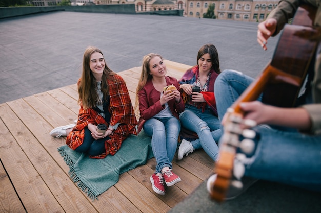 Fans on live music show. Friends leisure. Girls with fast food in hands listen singer's acoustic guitar improvisation.