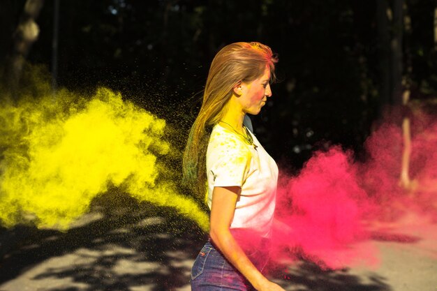 Fantastische blonde vrouw met levendige kleuren die om haar heen exploderen en poseren op het Holi-festival