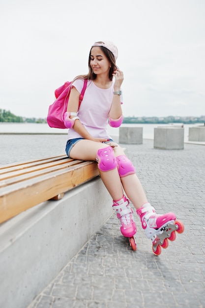 Fantastische jonge vrouw in casual kleding en pet zittend op de bank in het skatepark met rollerblades aan.