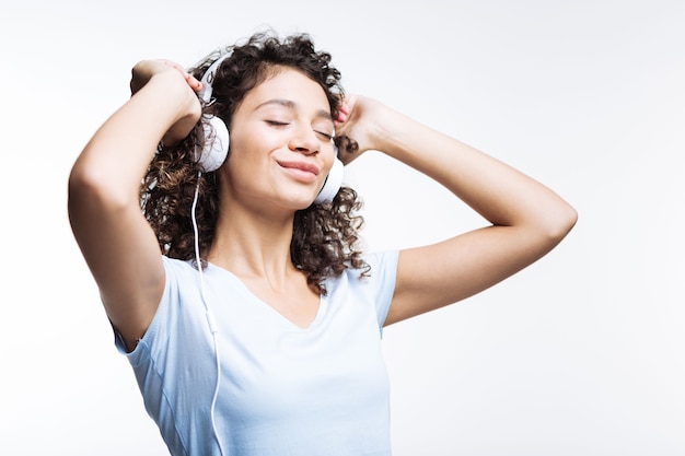 Fantastische muziek. Mooie curly-haired jonge vrouw luisteren naar de muziek in de koptelefoon en haar ogen sluiten, genieten van tracks