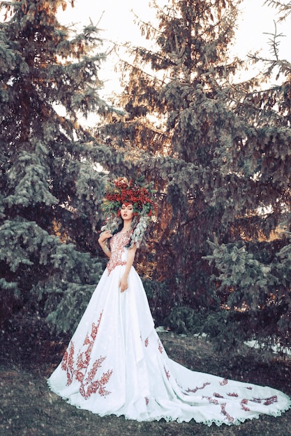 Photo fantasy winter queen standing in falling snow a beautiful woman in the crown of red berries