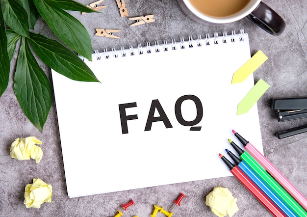 FAQ по тетради с чашкой кофе, сжатыми листами, мелками и степлером