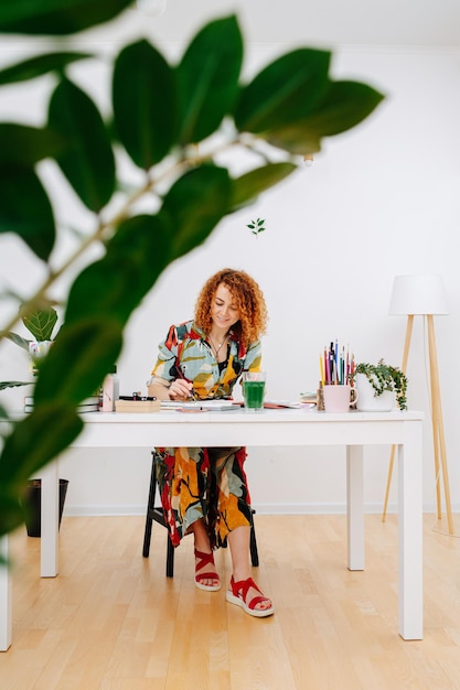 Far shot image of a woman with curly ginger hair drawing with a brush