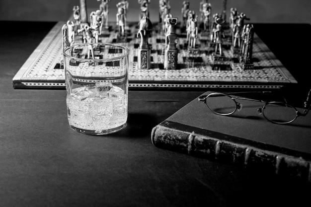 A Faraosstyle chess set with a book reading glasses and a drinking glass in black