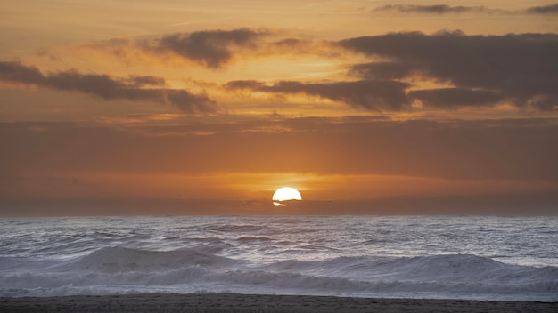 ポルト近くのポルトガルのビーチの海の水の後ろの地平線に太陽が隠れている日に別れを告げる