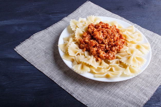 Farfalle bolognese pasta with minced meat on black wooden.