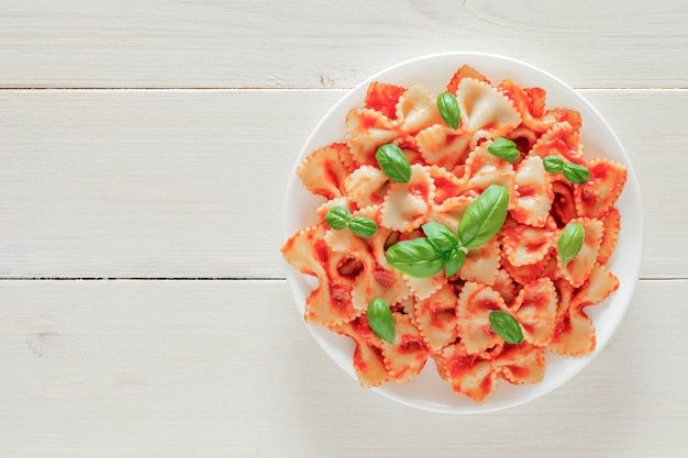 흰색 나무 보드 배경 상단 보기 공간에 있는 접시에 토마토 소스와 바질 녹색 잎을 곁들인 파르팔레 파스타 이탈리아노는 텍스트를 복사할 수 있습니다.