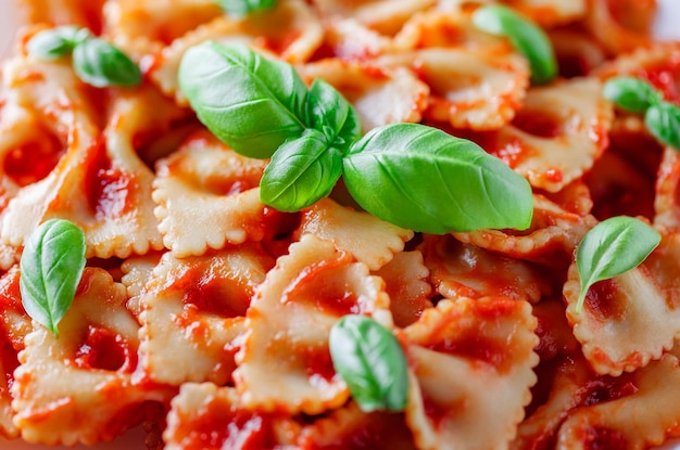 Farfalle cooked pasta with tomato sauce and basil green leaves closeup selective focus