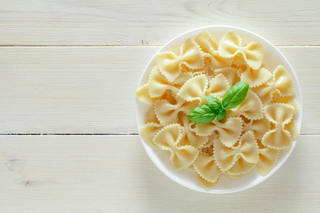 Farfalle gekookte pasta met basilicum groene bladeren op plaat op witte houten plank achtergrond bovenaanzicht ruimte om textxA . te kopiëren