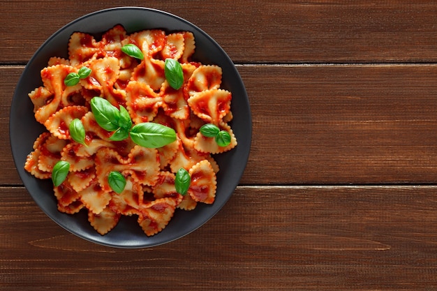 Farfalle gekookte pasta met tomatensaus en basilicum groene bladeren op plaat op houten bruine plank tafelblad achtergrond bovenaanzicht ruimte om textxA te kopiëren