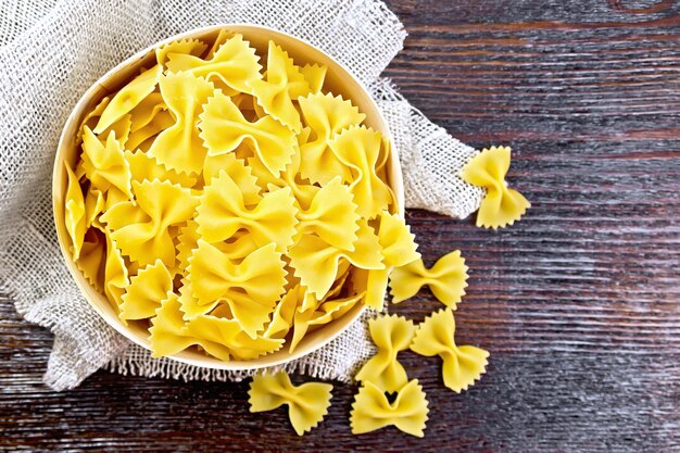 Farfalle pasta in bark box on a napkin of burlap on the background of wooden boards on top