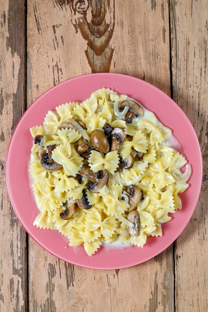 Farfalle pasta in een romige saus met champignons in een bord op een houten tafel