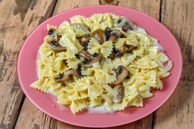 Farfalle pasta in een romige saus met champignons in een bord op een houten tafel