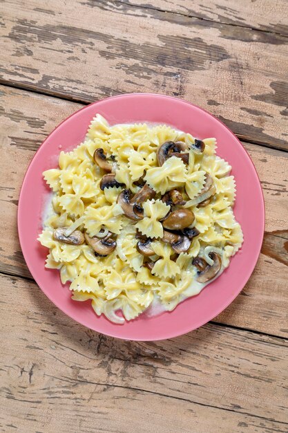 Farfalle pasta in een romige saus met champignons in een groot bord op een houten tafel