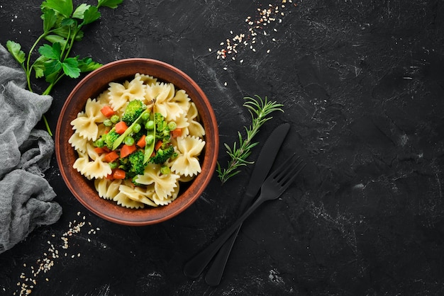 Farfalle pasta met groenten op het bord Bovenaanzicht Op een zwarte achtergrond Gratis kopieerruimte