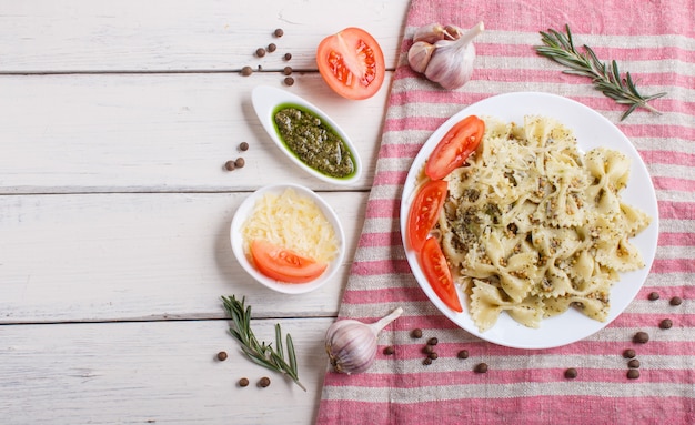 Farfalle pasta met pesto saus, tomaten en kaas op een linnen tafellaken op wit