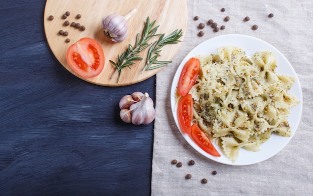 Farfalle pasta with pesto sauce, tomatoes and cheese on a linen tablecloth on black