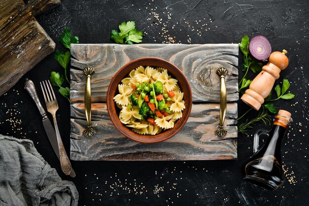 Farfalle pasta with vegetables on the plate Top view On a black background Free copy space