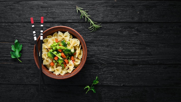 Farfalle pasta with vegetables on the plate Top view On a black background Free copy space