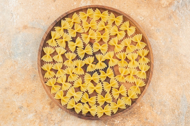 Pasta farfalle su un piatto di legno sulla superficie blu