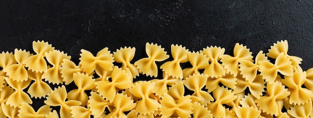 Farfalle rauwe pasta op zwarte betonnen achtergrond. Koken concept. Bovenaanzicht met kopie ruimte.