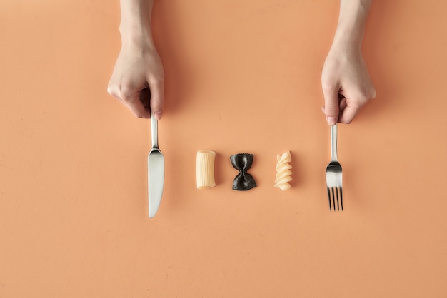 Farfalle, tortiglioni and fusilli pasta and hands with fork and knife