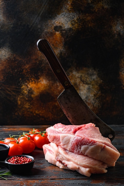 新鮮な豚バラ肉、素朴なテーブルの上で木製の暗い板の上でグリルまたは調理するためのオイルとスパイスを使った生の豚バラ肉、チョッピングクリーバーブッチャーナイフ、側面図